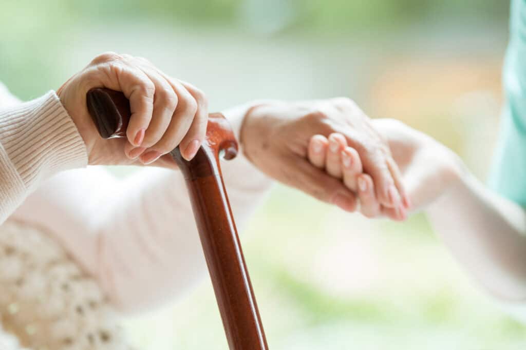 close up of elderly lady's hand holding a cane and a friend's hand