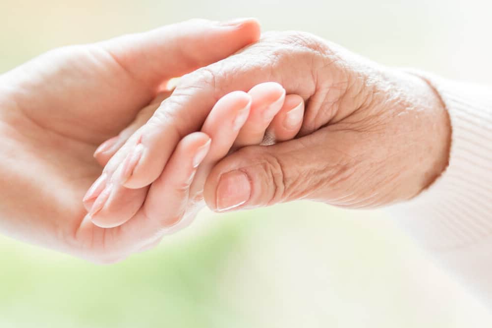Close-up of tender gesture between two generations. Young woman holding hands with a senior lady. Blurred background