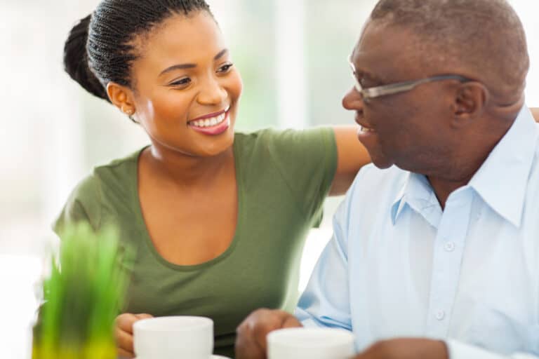 smiling elderly african american man enjoying coffee with his granddaughteer at home