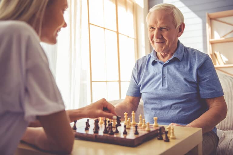 Happy grandfather playing chess with his adult granddaughter